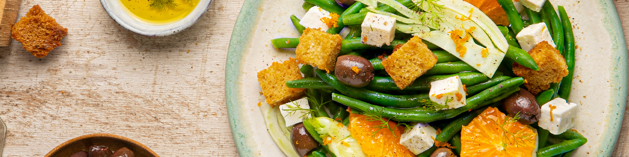 ingredienti e preparazione per l’insalata di Fagiolini Primavera con feta, arancia, olive taggiasche e crostini di pane.